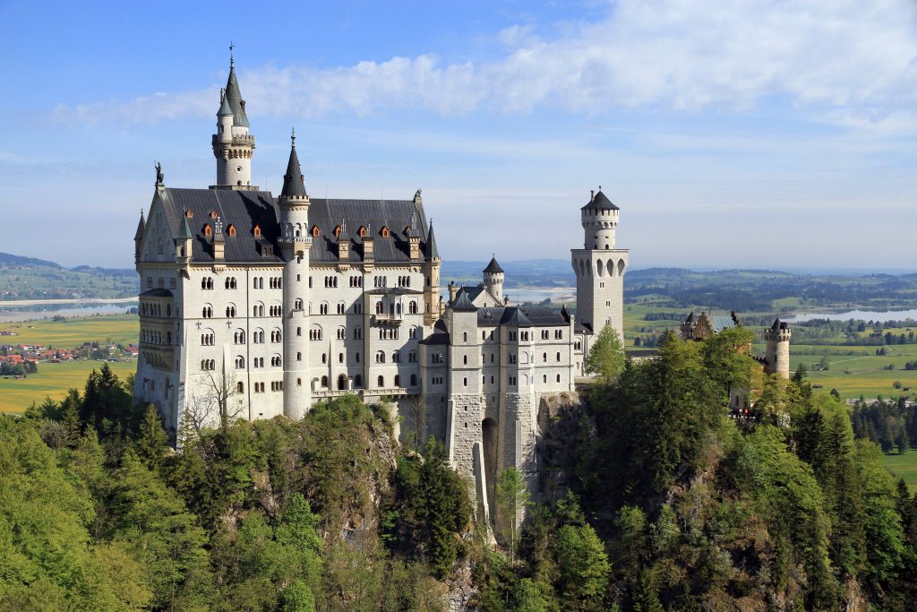 Castillo blanco de Neuschwanstein sobre un monte boscoso, con torres puntiagudas y el cielo azul